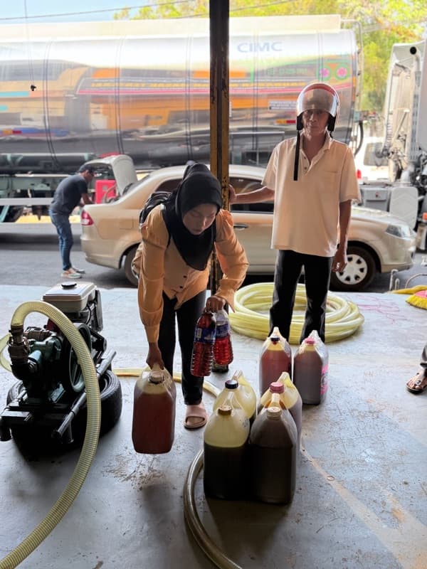 An MSR worker pumping used cooking oil from jerry cans into a truck