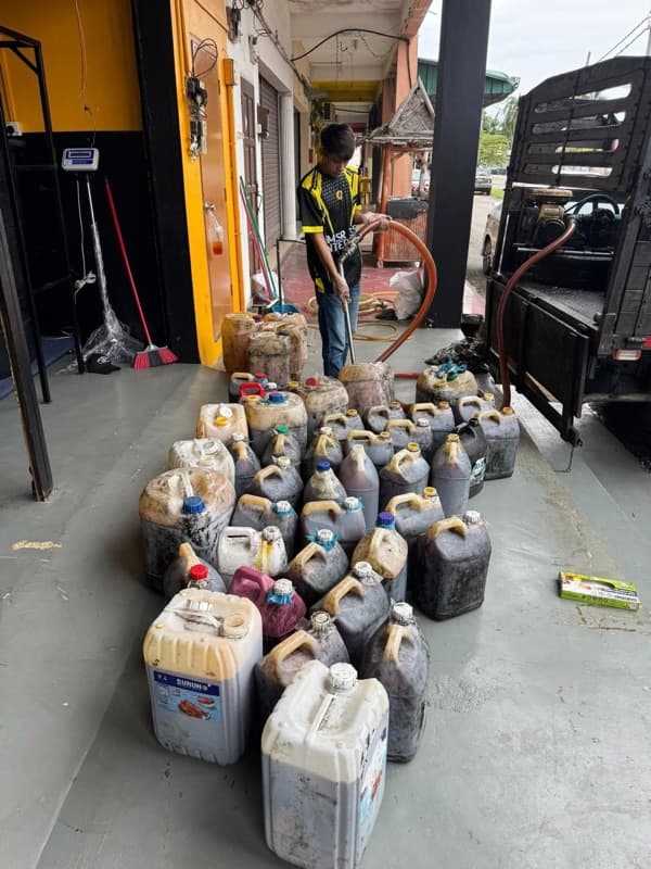 Used cooking oil bottles in front of a pump and a black tank at the warehouse