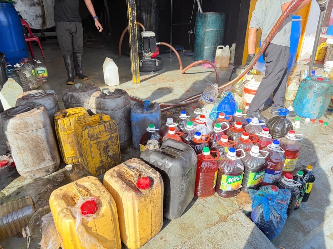 Customers' jerry cans and bottles of used cooking oil beside pump hoses