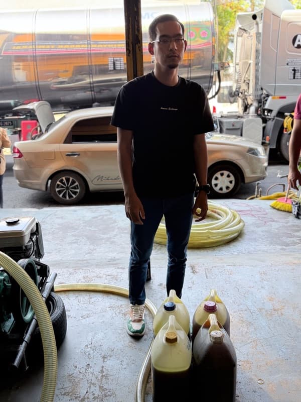 A customer standing beside jerry cans of used cooking oil he delivered