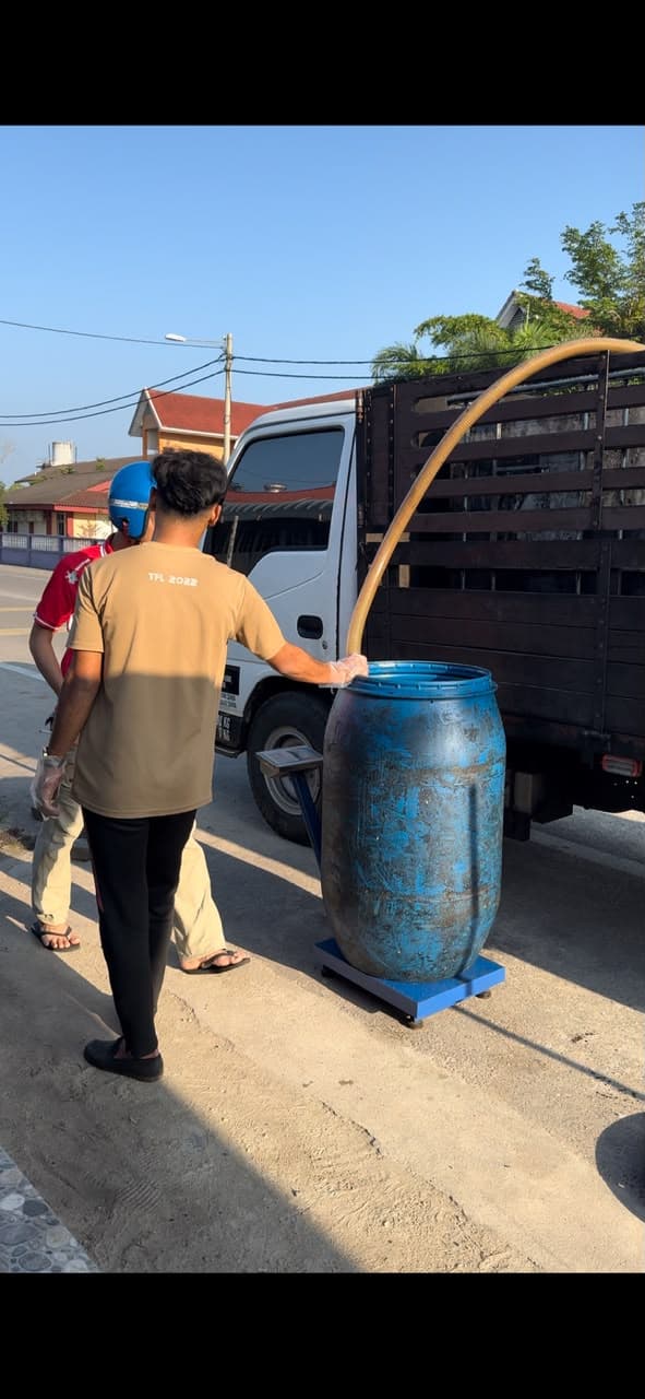 An MSR staff member pumping used cooking oil from a blue drum on a scale into a truck