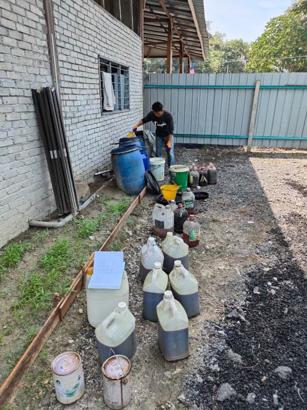 An MSR staff member pouring used cooking oil into a blue drum among customers' bottles and containers